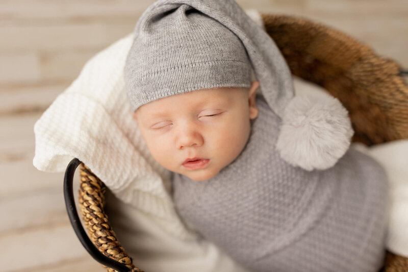 Newborn baby boy in a grey wrap and hat sleeping in a basket