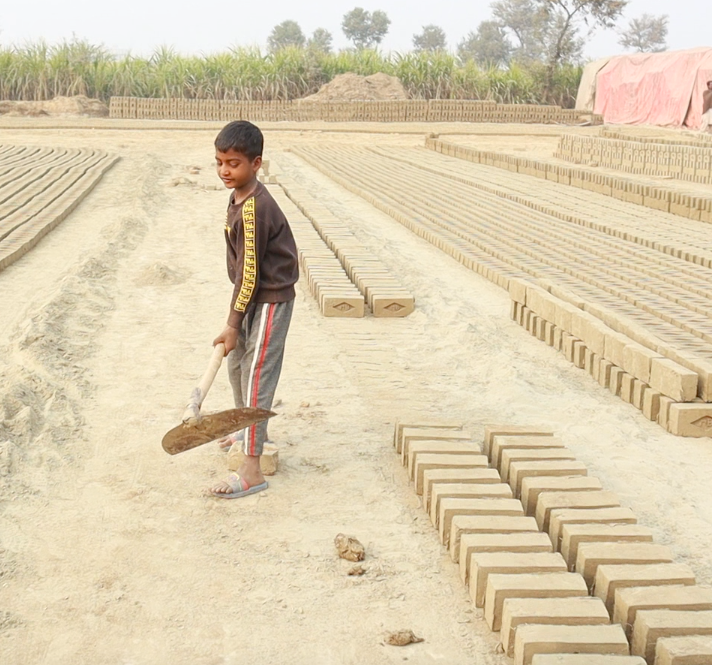 An enslaved young child works at the kiln shoveling dirt for the bricks.