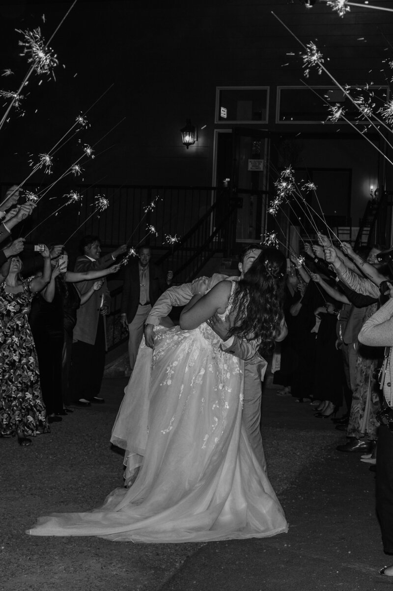 A couple shares a romantic dip kiss during their sparkler exit at The Empress Estate, surrounded by guests and a magical nighttime wedding atmosphere.