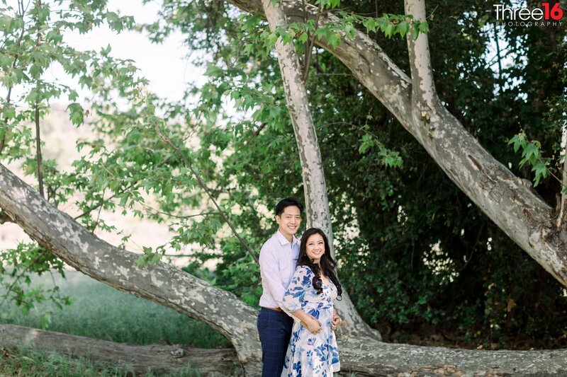 Groom to be holds his Bride from behind next to a large tree at the Ronald W. Caspers Wilderness Park