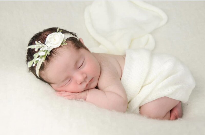 Baby girl posed on stomach wrapped in a cream-colored soft throw. 