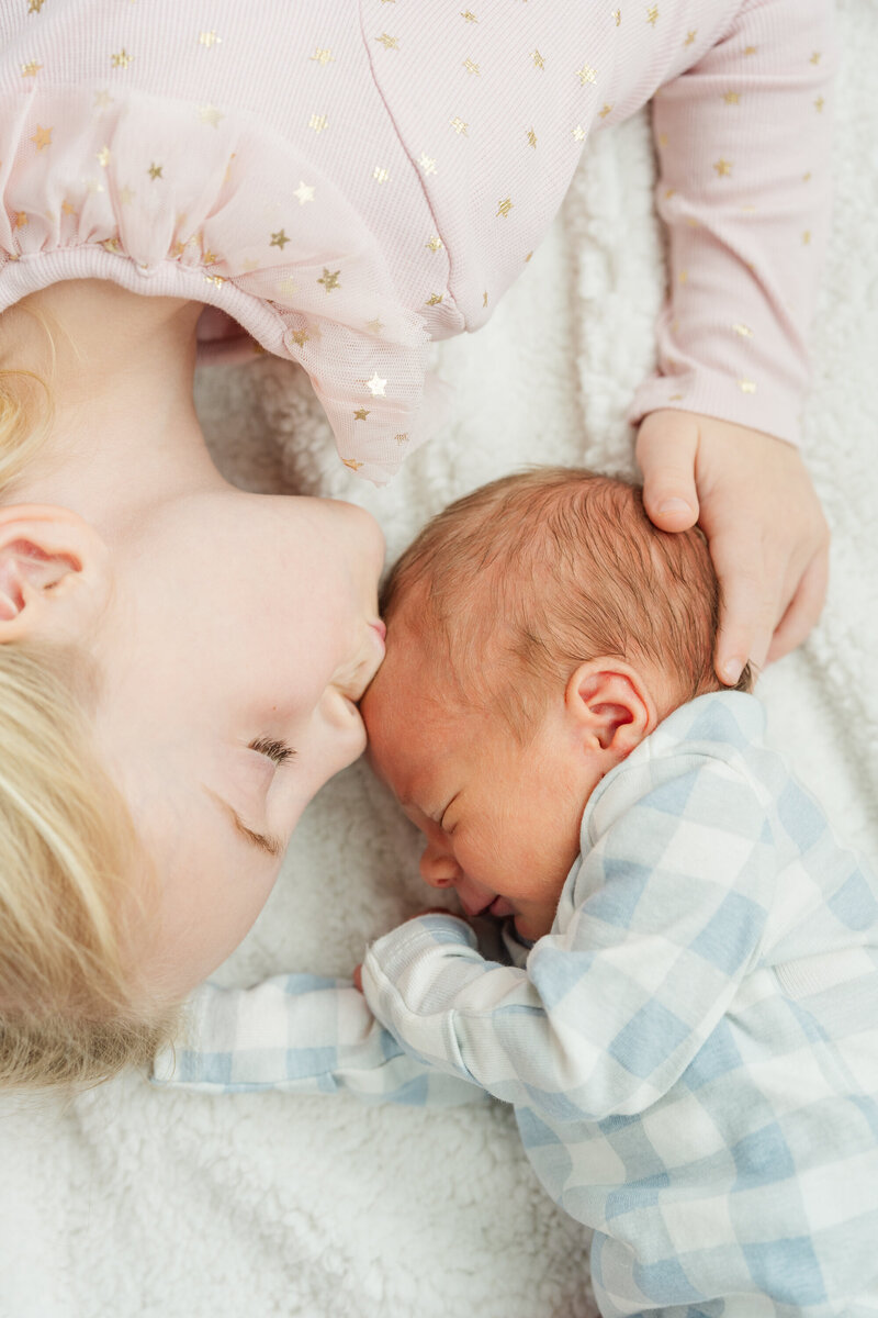 older sibling kisses her newborn baby brothers head