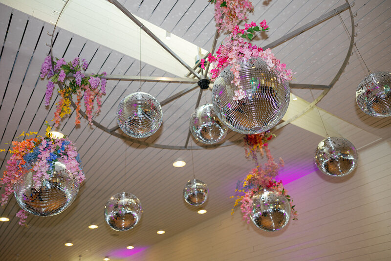 Disco balls and colorful flowers hanging from ceiling at reception planned by Bianca Nichole and Co
