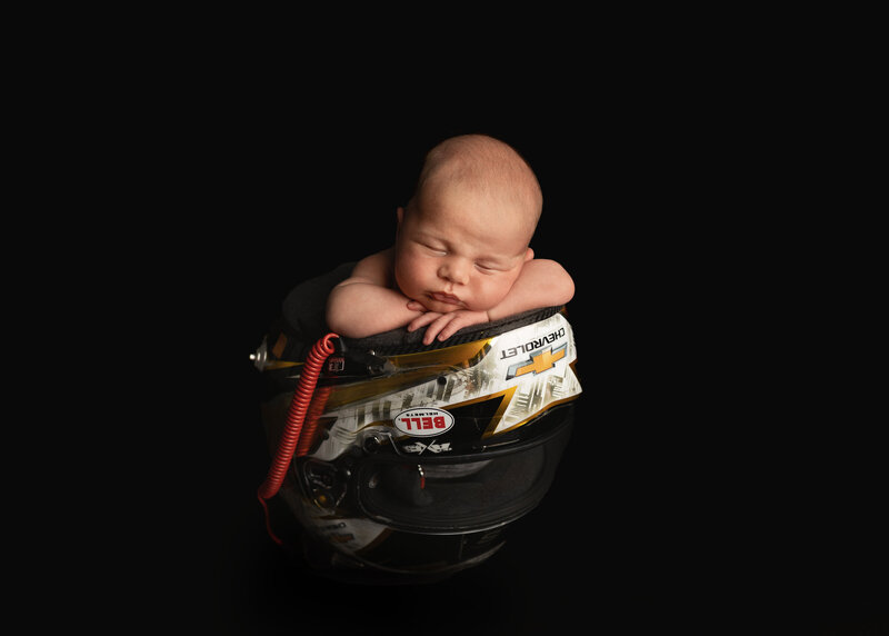 Newborn baby in daddy's nascar helmet at newborn photography session