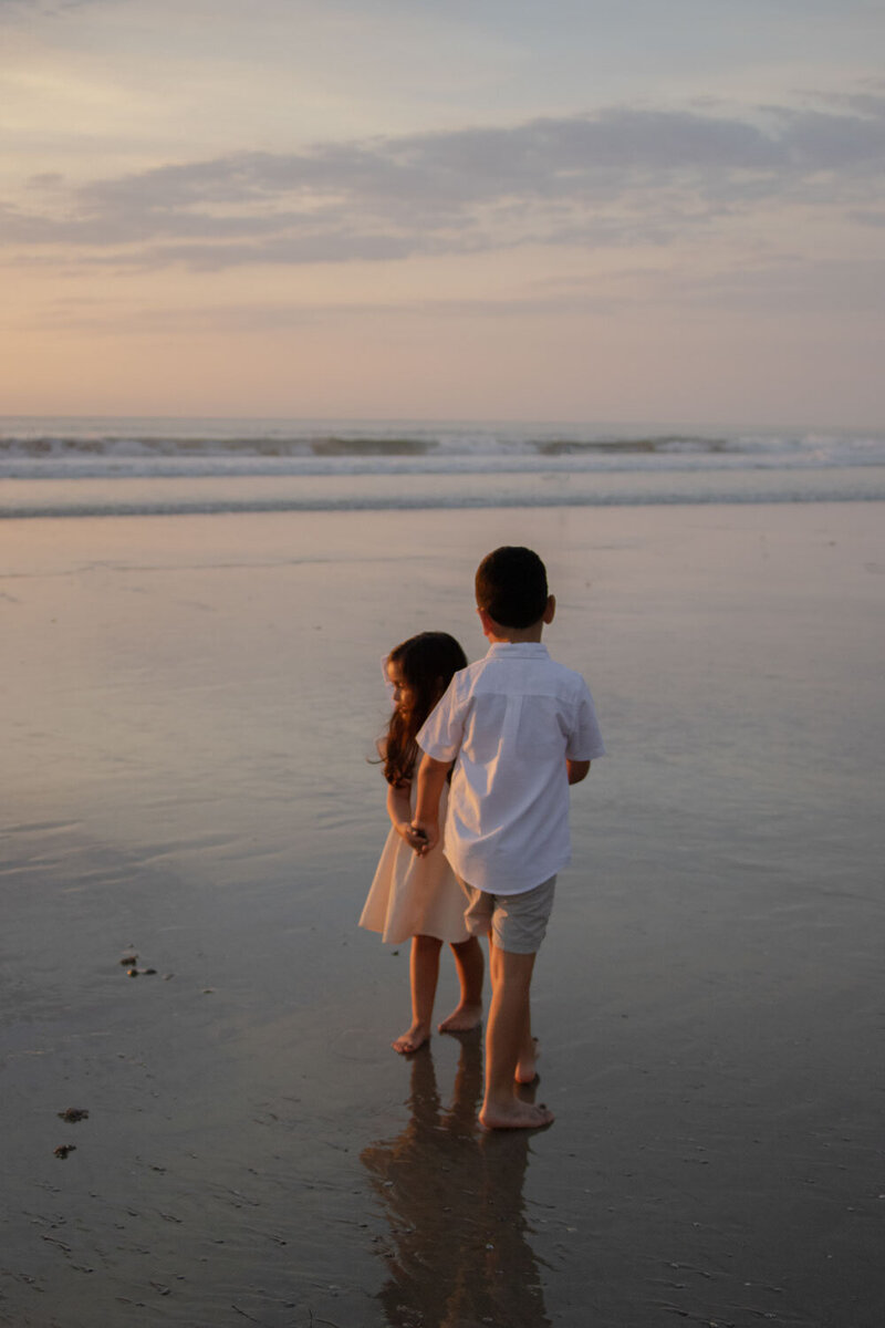 Two children standing by the water's edge at sunset