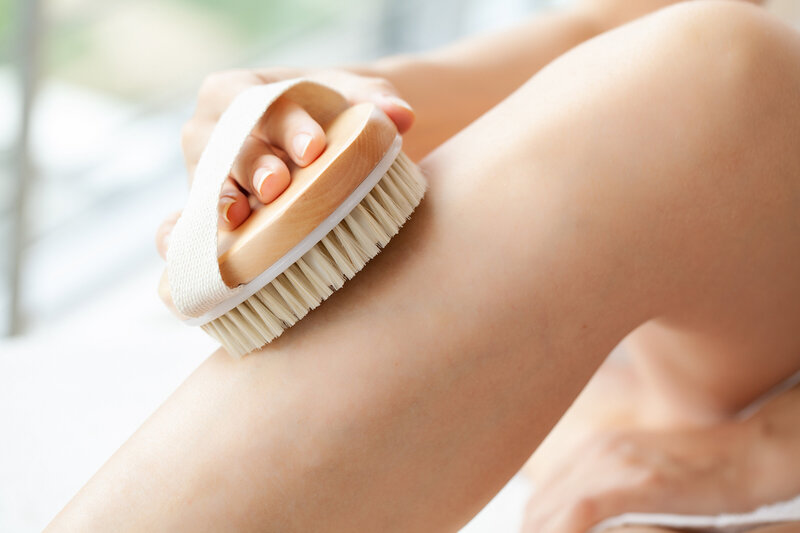 Close-up of a dry brush being used on a person’s leg — body exfoliation technique