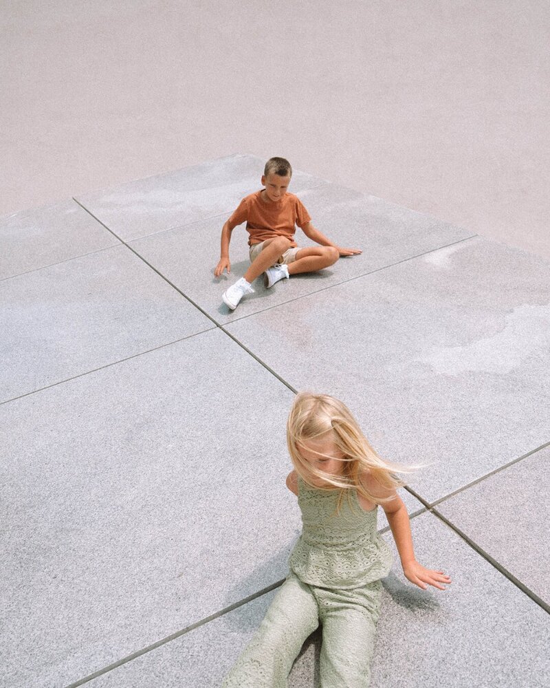 Brother and sister sitting on modern stone tiles during a Costa Mesa family photo session, styled in earthy tones.