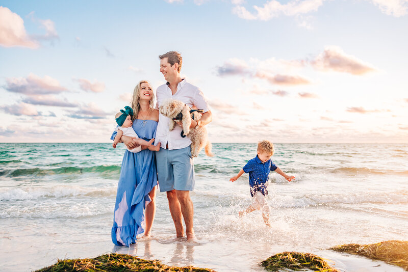 A family of four posing for a beach portrait at sunset, with the St. Petersburg skyline in the background.