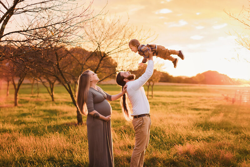 maternity couple throw older sibling in air during sunset