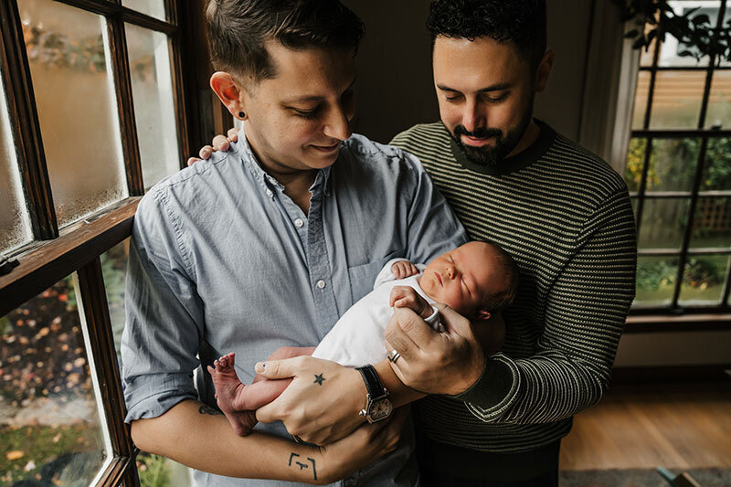 two dads hold their newborn baby