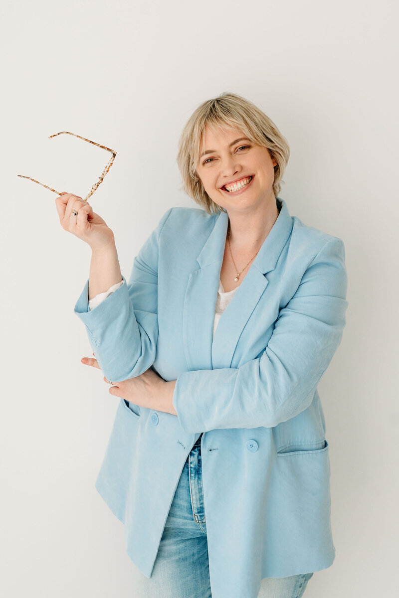 Rosanne van Cruijningen, van Rosanne Sarah freelance redactie en schrijfcoaching, kijkt lachend de camera in met bril in haar hand.