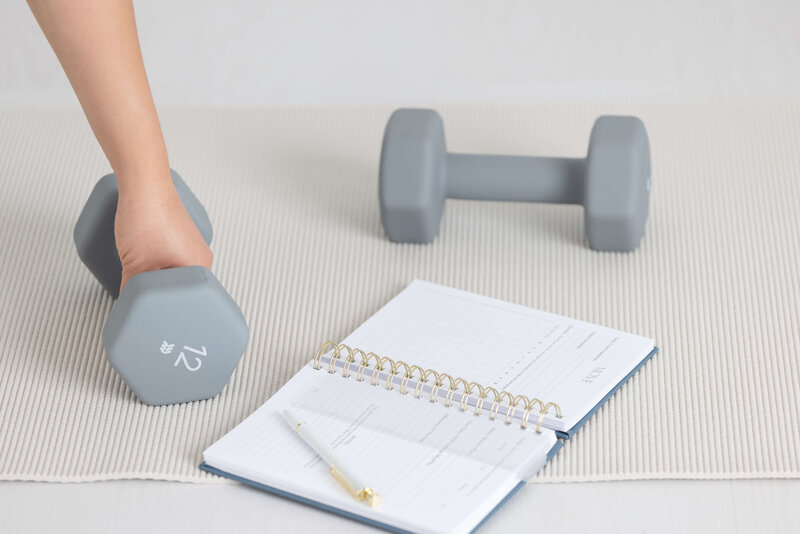 hand reaching for gray dumbbell  and fitness journal open next to it