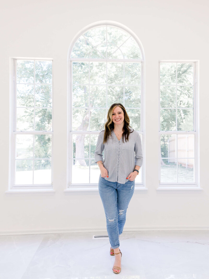 woman in bright entryway wearing blue jeans and smiling