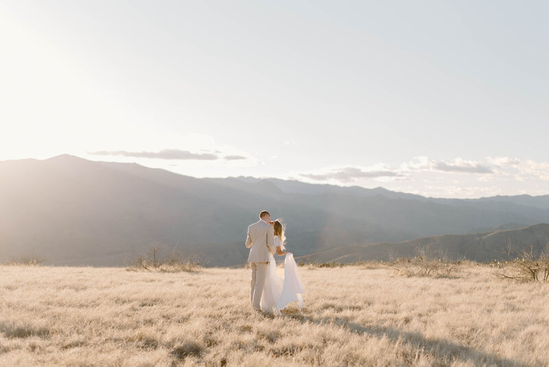 Couple dancing in a wheat field wearing their bridal attire