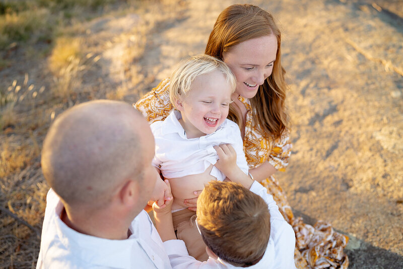 Joyful family moment during golden hour in Geelong, with parents and siblings playing and laughing together in a sunlit natural setting.