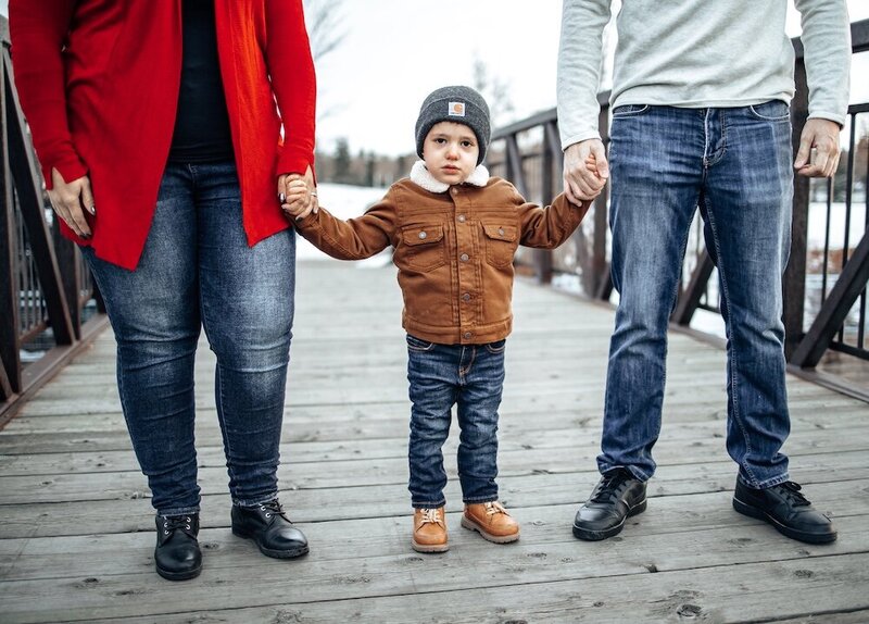 a mom and dad hold their sons hand on a bridge in the winter in Edmonton