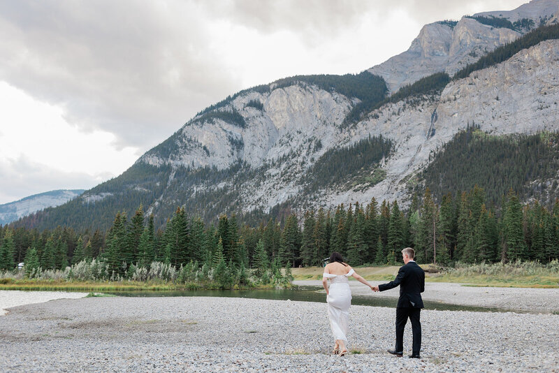 Couple holding hands and walking on rock beach in the Canadian rocky mountains