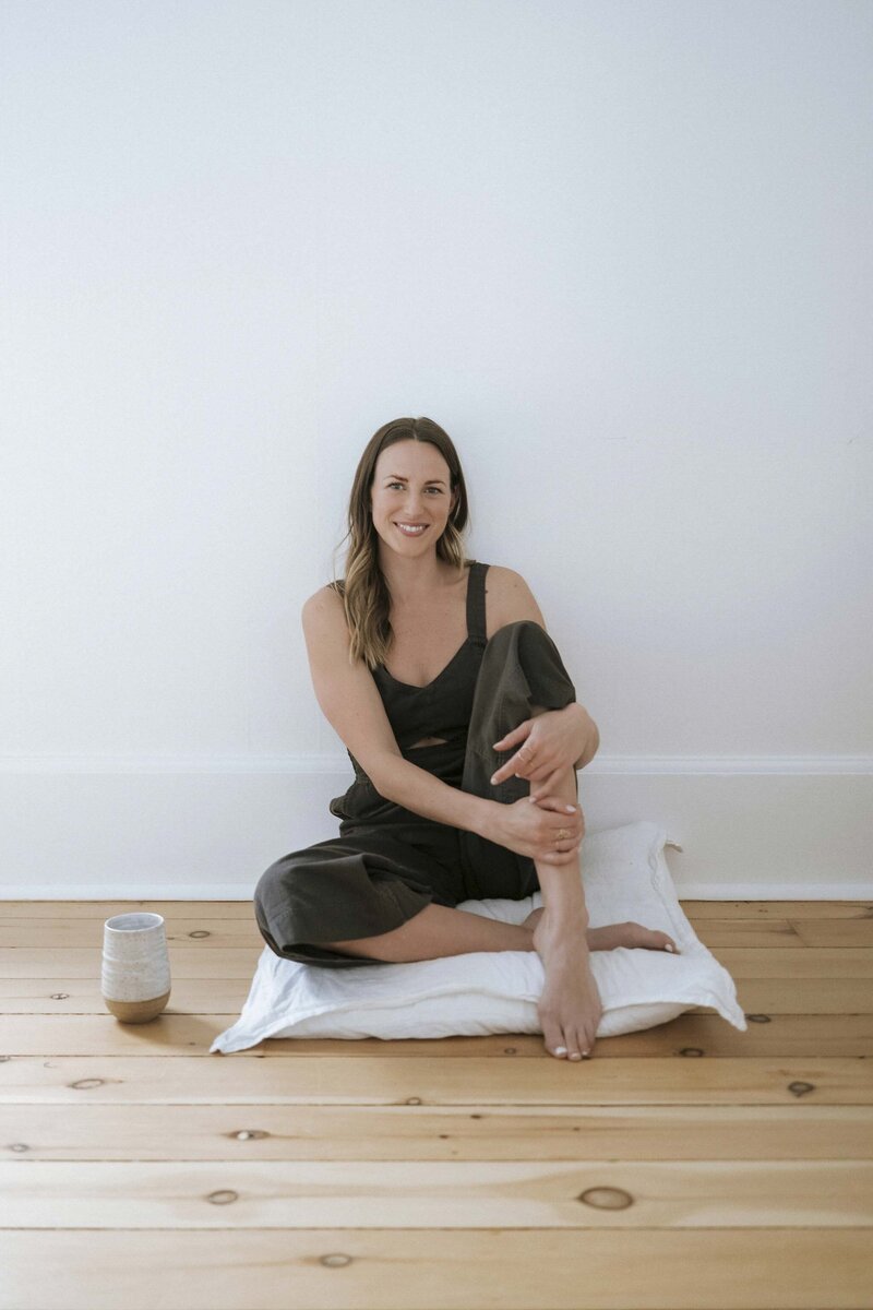 Kaylyn Gelata sitting comfortably on a white cushion, smiling with a cup of tea beside her.