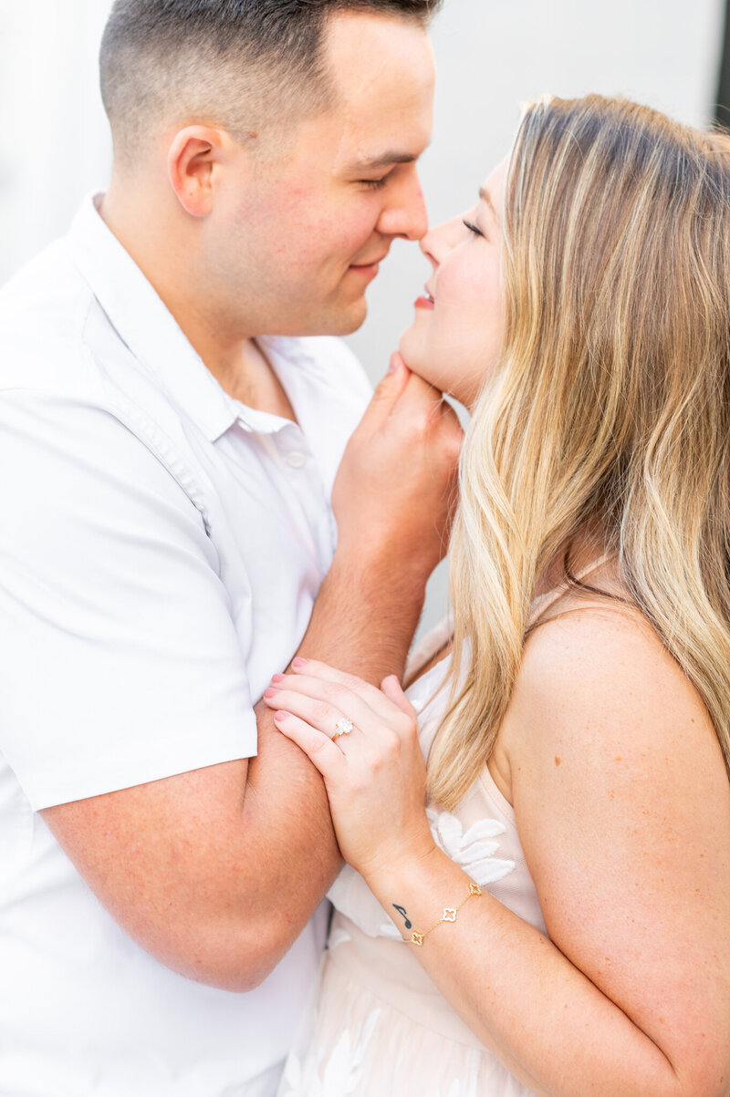A close up of a man holding the chin of a woman. She his holding her arm and their are looking into each others eyes, smiling.