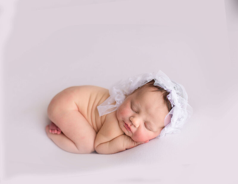 Infant posed on white fabric with lace bonnet