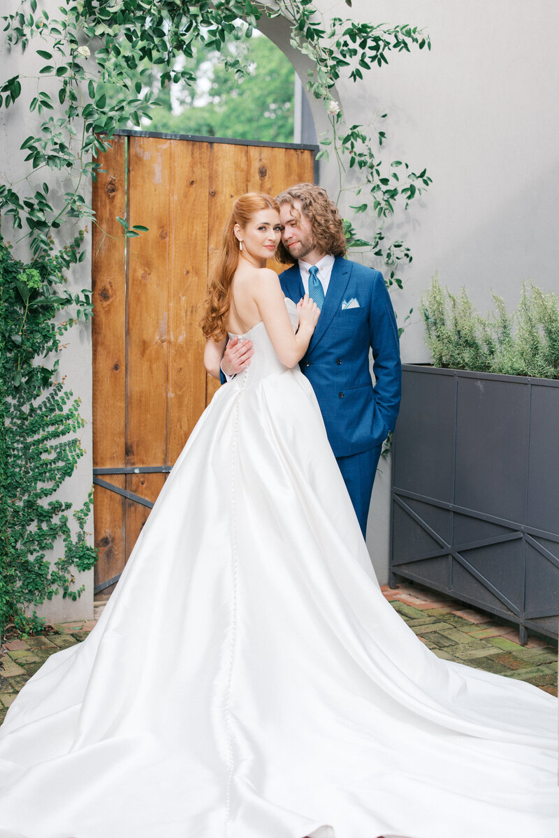 Bride with back of dress fanned out looks over shoulder holding grooms lapel while he snuggles into her temple