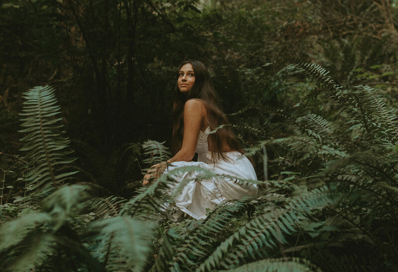 girl in white dress sitting among forest ferns