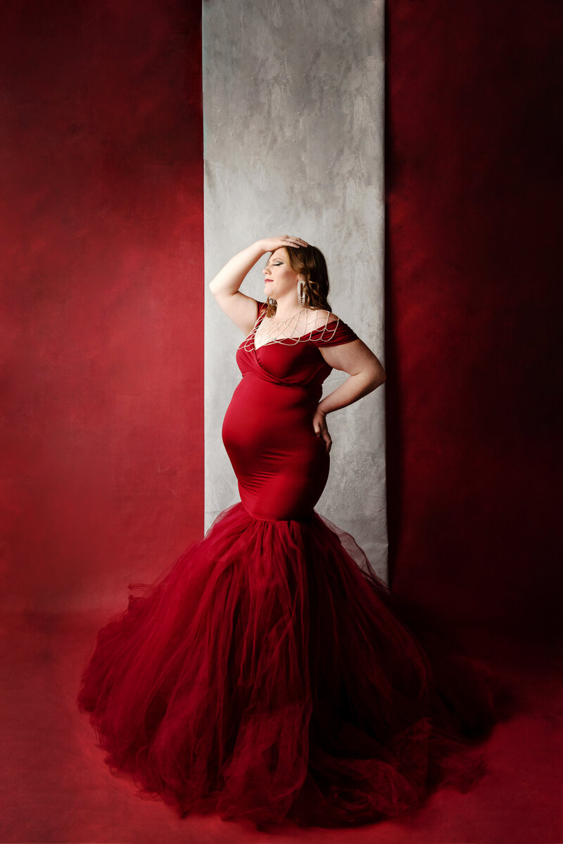 st-louis-maternity-photographer-mom-in-red-mermaid-gown-with-tulle-with-red-and-gray-backdrop