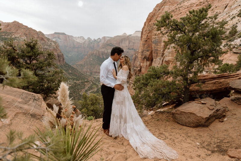 bride hugging the back of her grooms neck surrounded by red rock formations in Utah at sunset