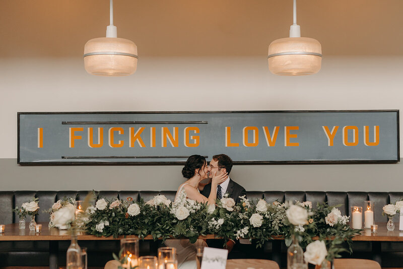 Couple kissing under sign that says "I fucking love you" at Olive and Oak in Webster Groves