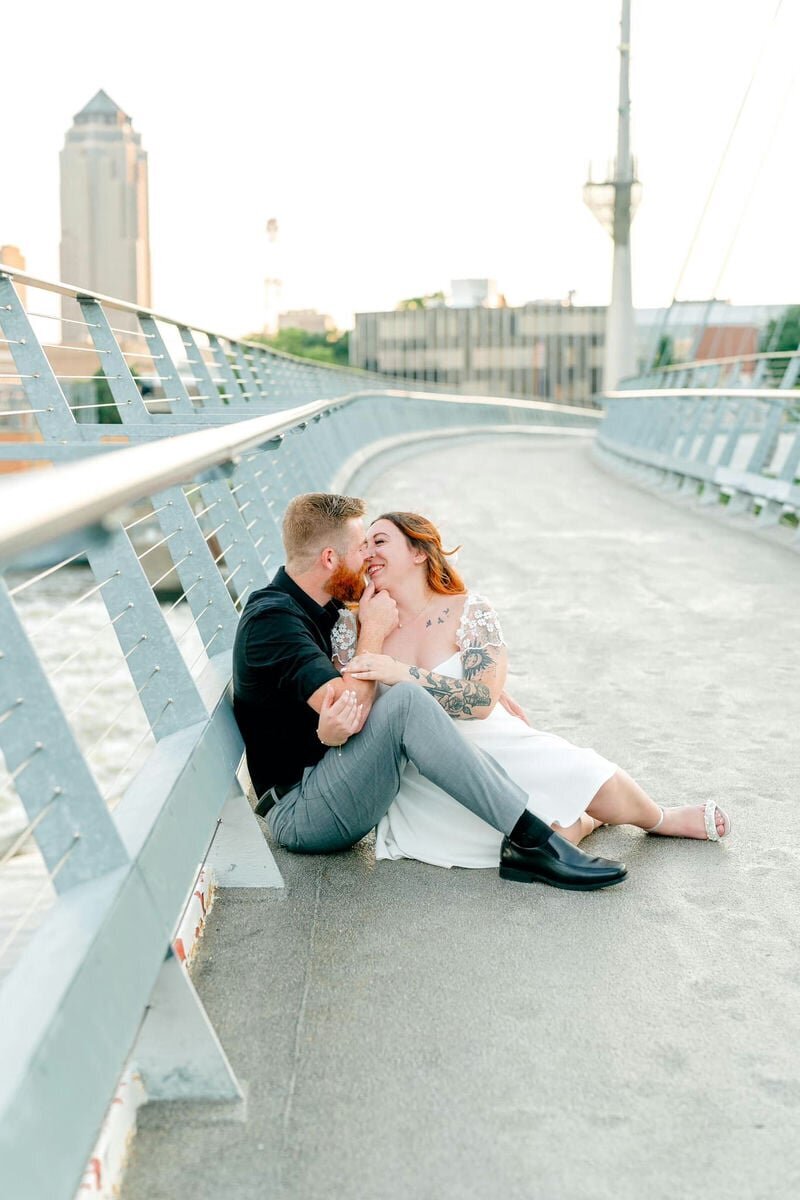 A couple embracing outdoors, with the man gently leaning his forehead against the woman's. The woman is wearing a navy off-the-shoulder dress and smiling.