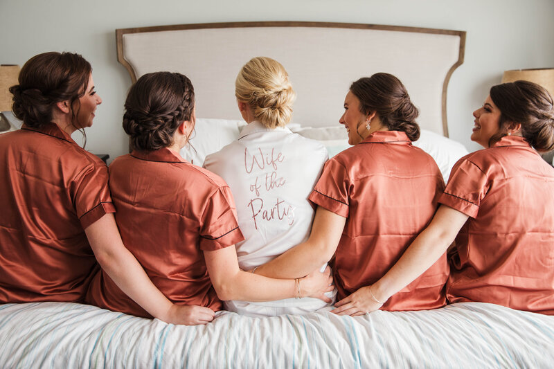 bride sitting on bed with bridesmaids wearing matching pajamas
