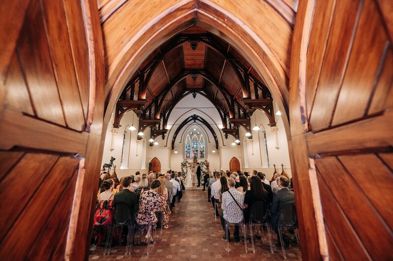 a wedding ceremony inside the rose historic chapel in christchurch, an old church with wooden doors available for hire