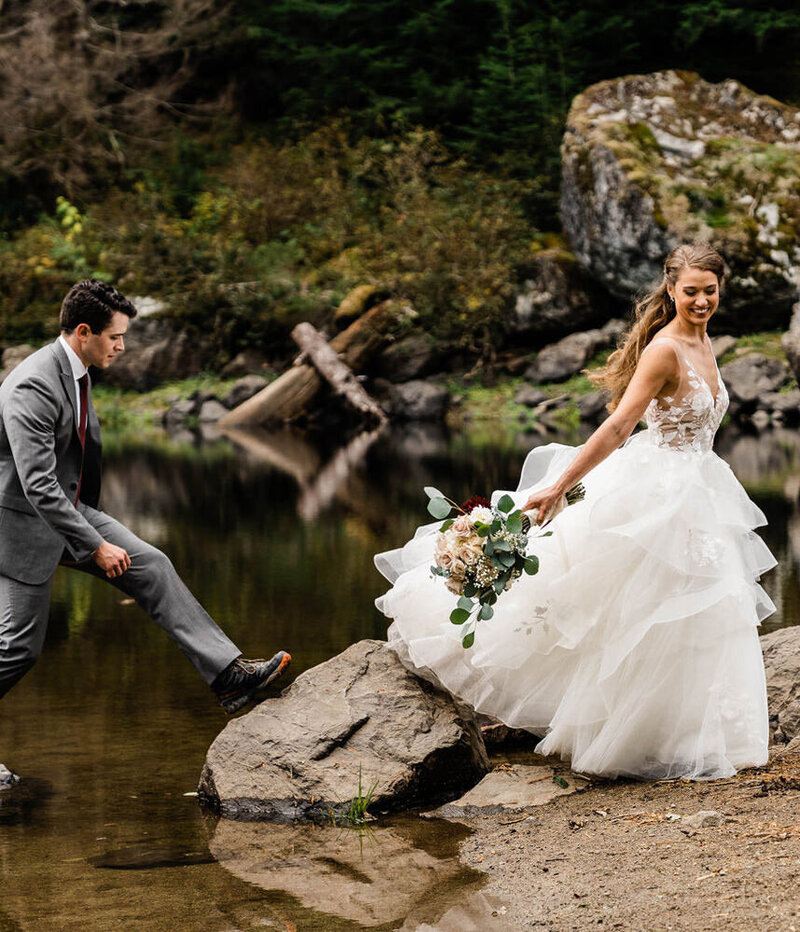 A bride and groom walk over rocks on a crystal clear backcountry lake in the Washington cascades photographed by pacific northwest elopement photographer amy galbraith