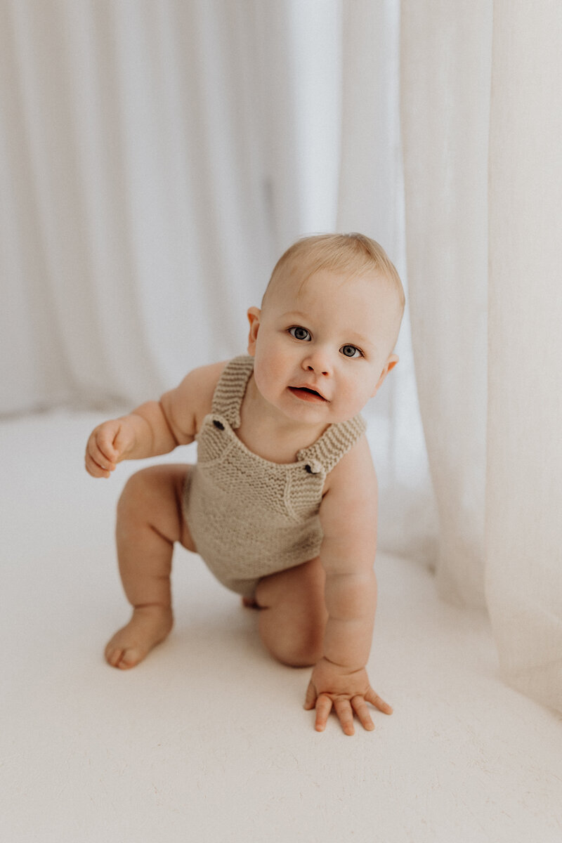 A little boy crawling towards the camera during his milestone photoshoot, hes wearing a cute onesie and has a cute smile