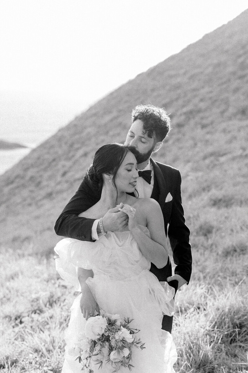 black and white photo of a groom lifting his bride and twirling her on the beach