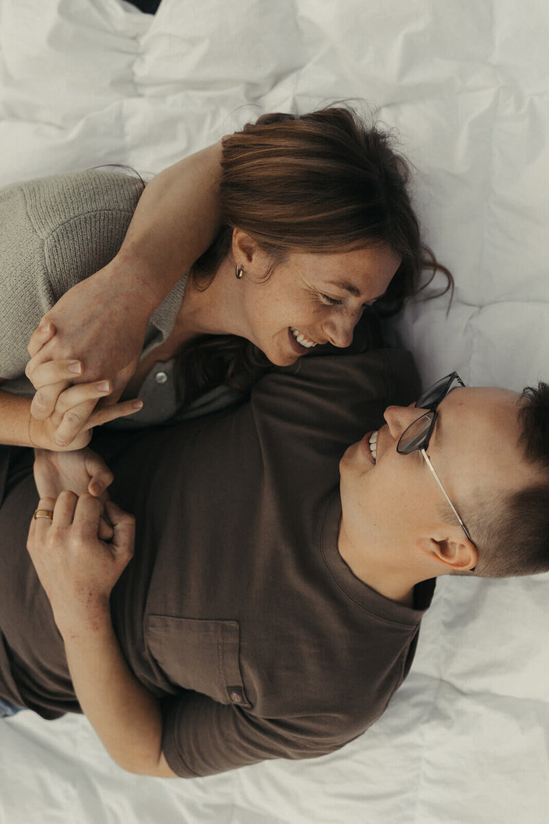 Candid wedding photographer lays in white duvet with her husband
