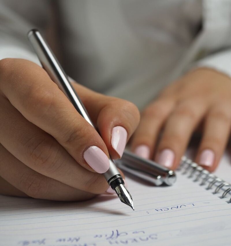 Close-up of a woman writing in a notebook with a silver pen, representing the initial assessment phase of personalised fertility nutrition support.