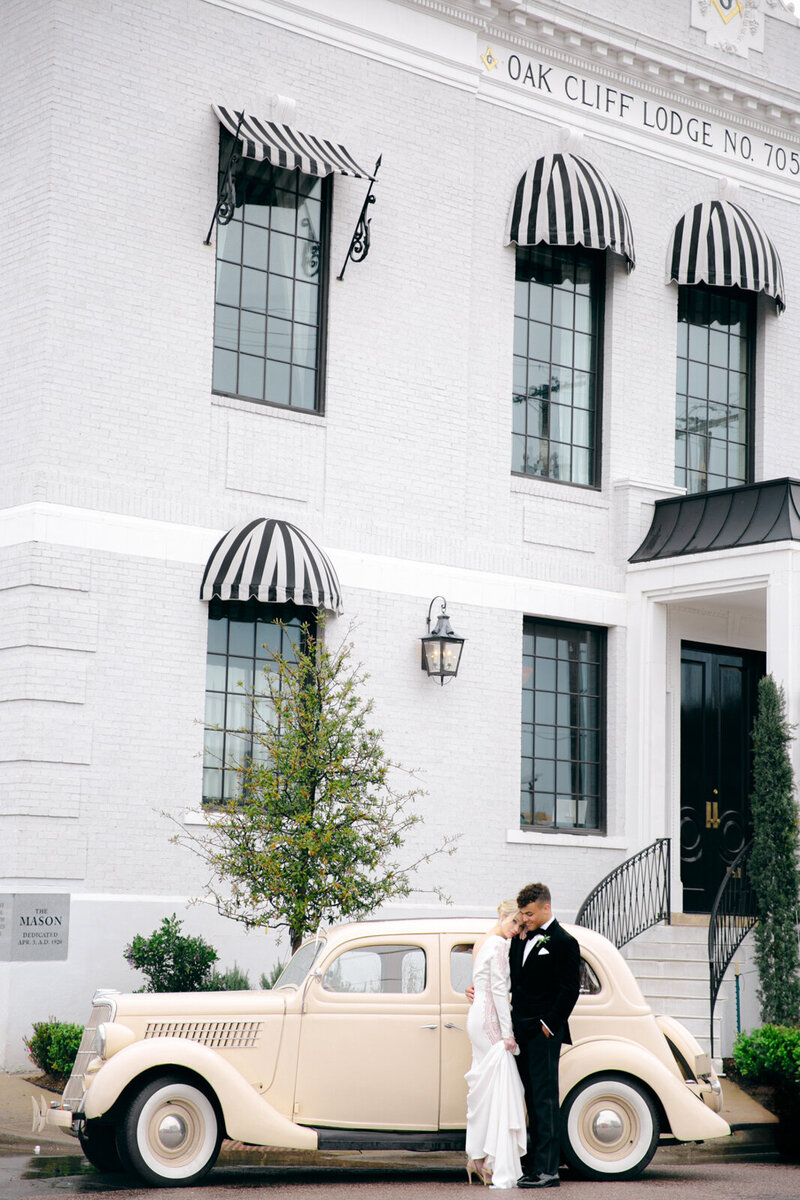 Bride and groom posing with a vintage car in front of The Mason wedding venue in Dallas.
