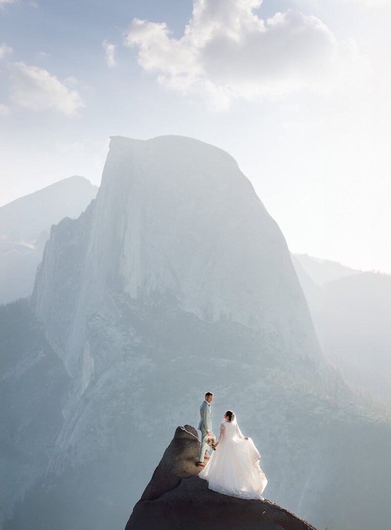 A bride and groom standing in front of half dome from the view at Glacier Point n Yosemite National Park. 