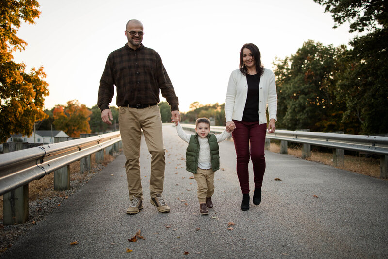 Toddler boy walking down the road holding grandparent's hands as the sun sets