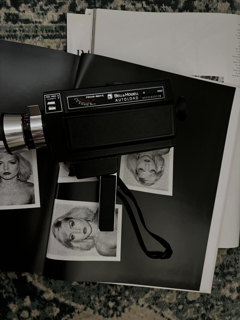 An old black camera standing on top of black and white polaroid images of a woman and some files. Rodeo PR brand photos