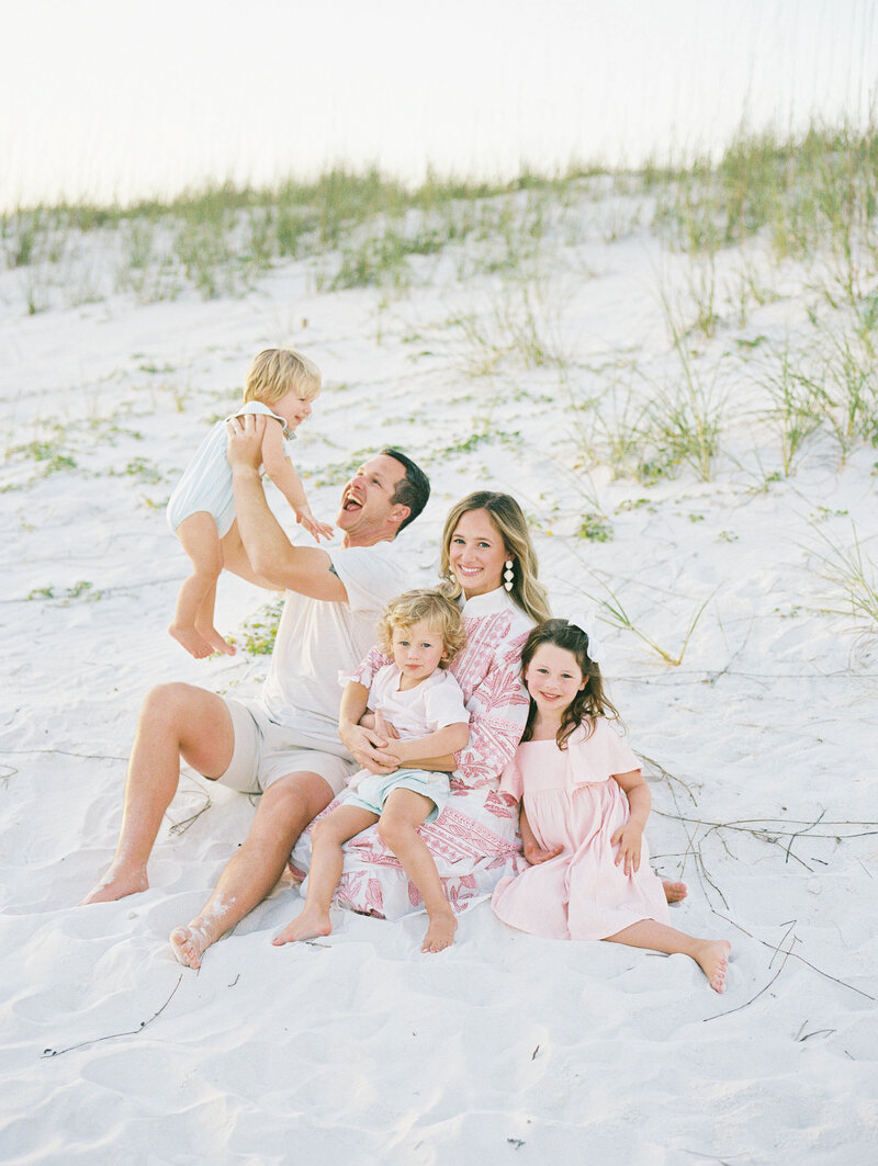 Family of five sitting on the sand and smiling together