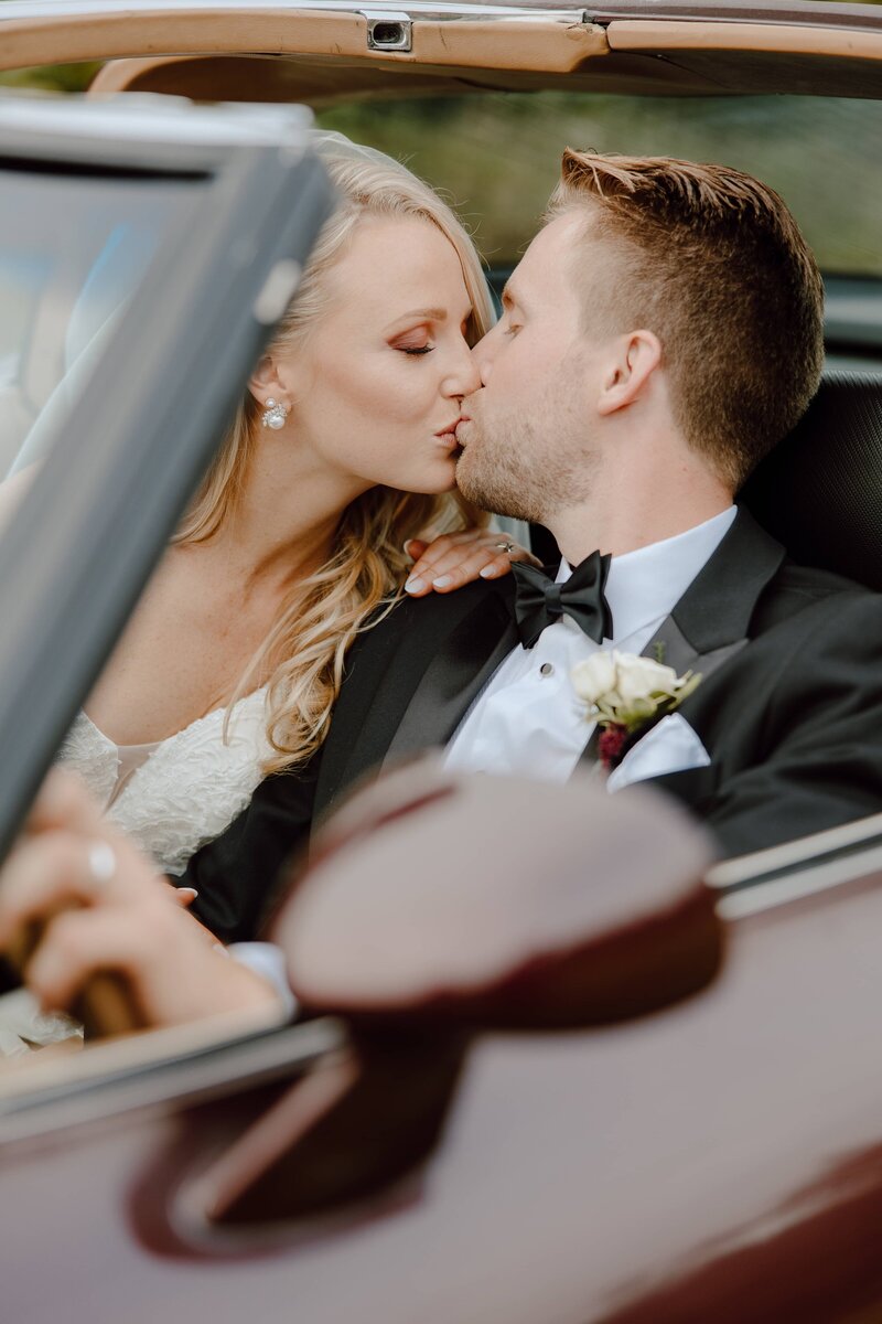 bride and groom sitting in car kissing
