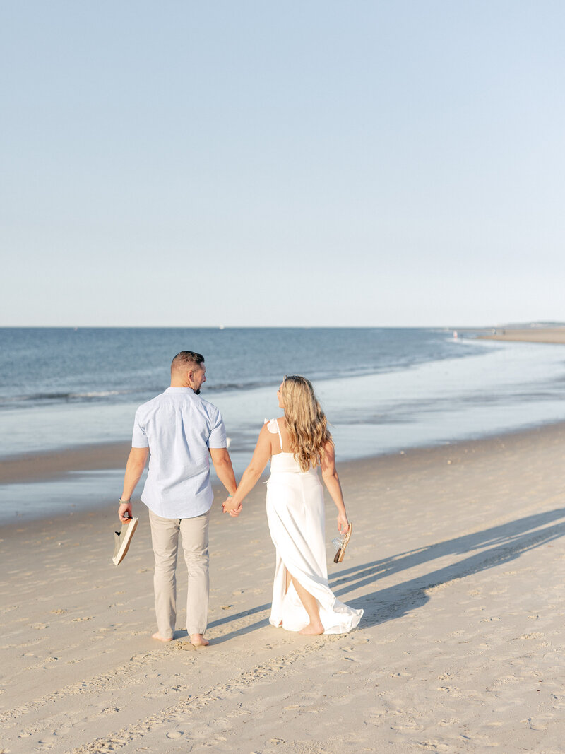 Couple holding hands and walking barefoot on the sand in front of the ocean