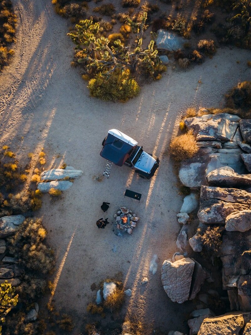 Aerial view of an exclusive overland camping setup with a Jeep and campfire in a hidden desert location, part of a curated luxury adventure experience