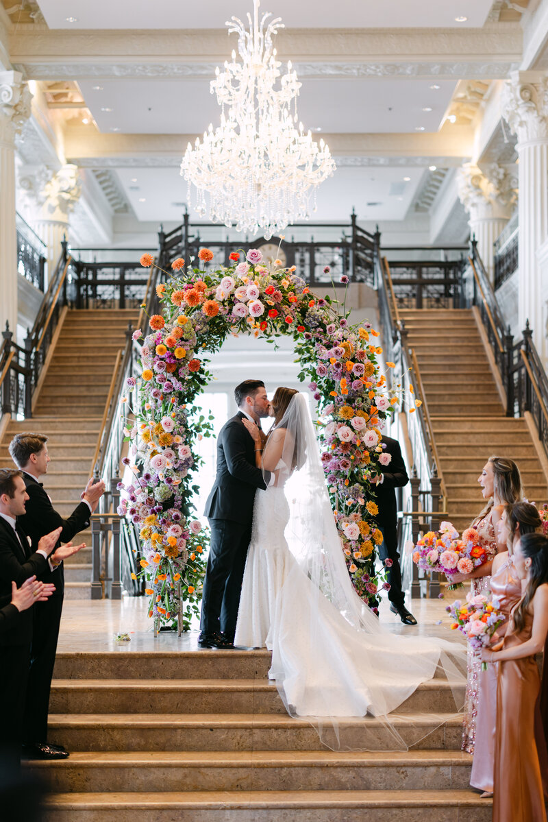 Bride and groom standing in front of a lush floral arch