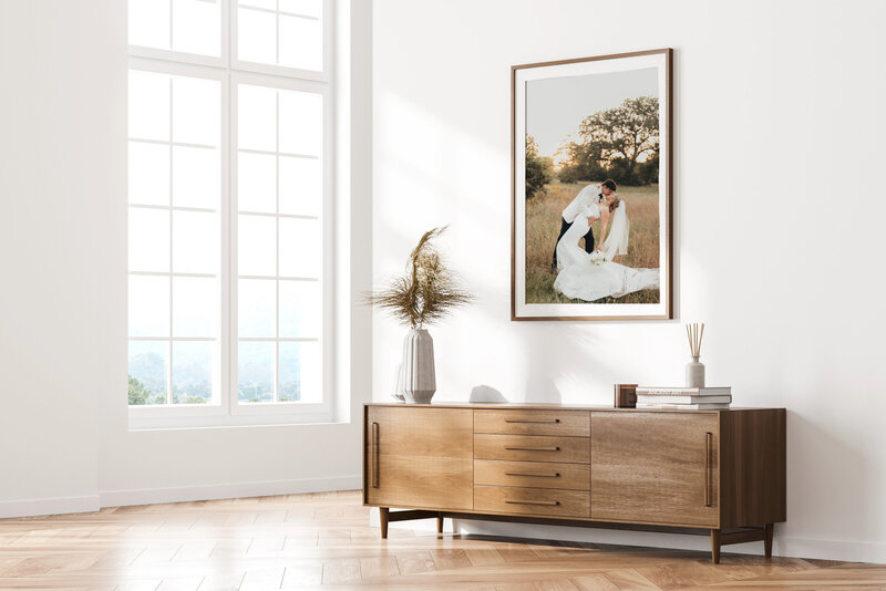 artwork mockup of a wedding portrait on a white wall, with neutral toned dresser and a large window.