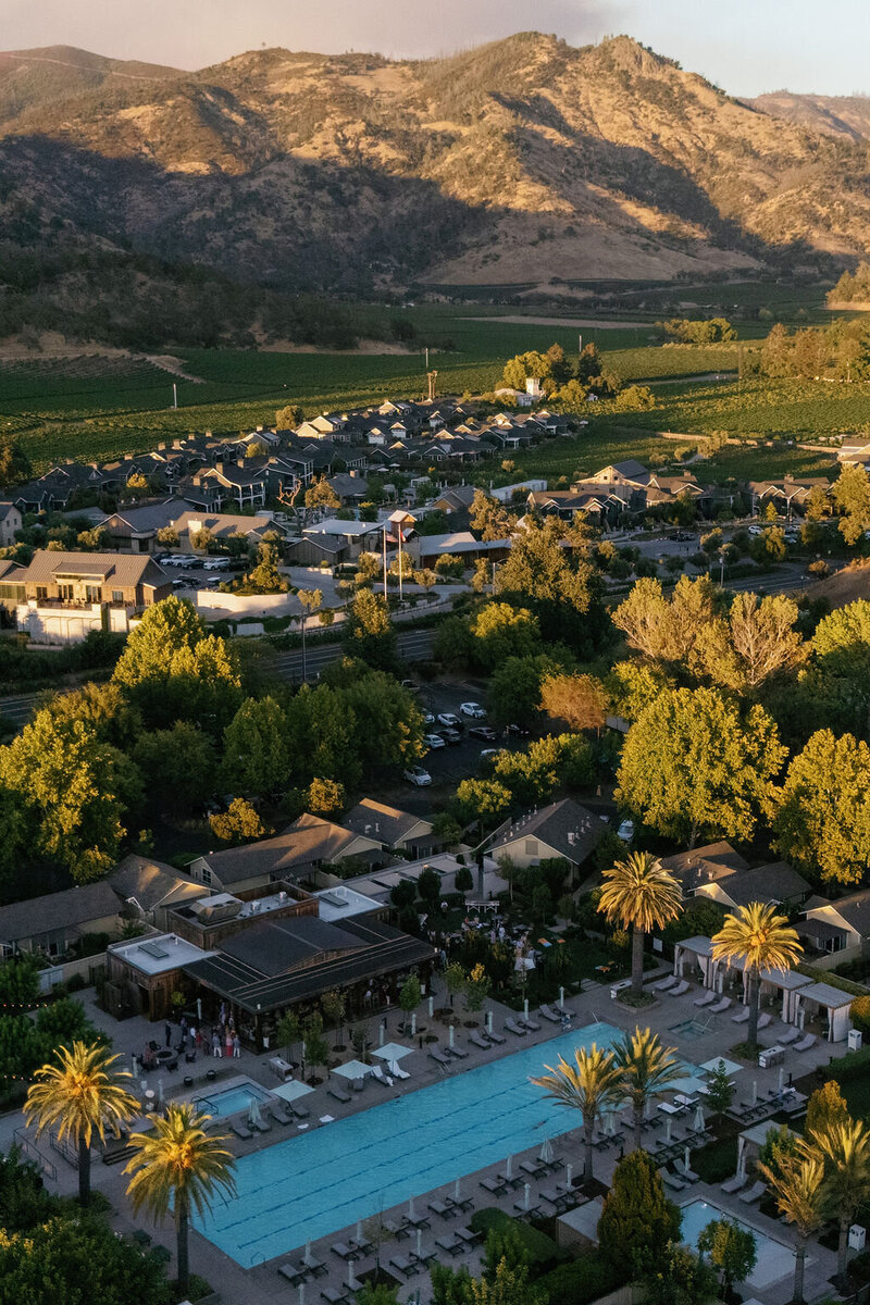 A bride and groom share a joyful moment pouring champagne into a tower of glasses, adorned with figs and grapes.