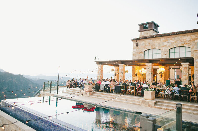 A breathtaking wedding reception setup at a hillside venue, featuring elegant string lights, long tables, and guests enjoying a romantic evening.
