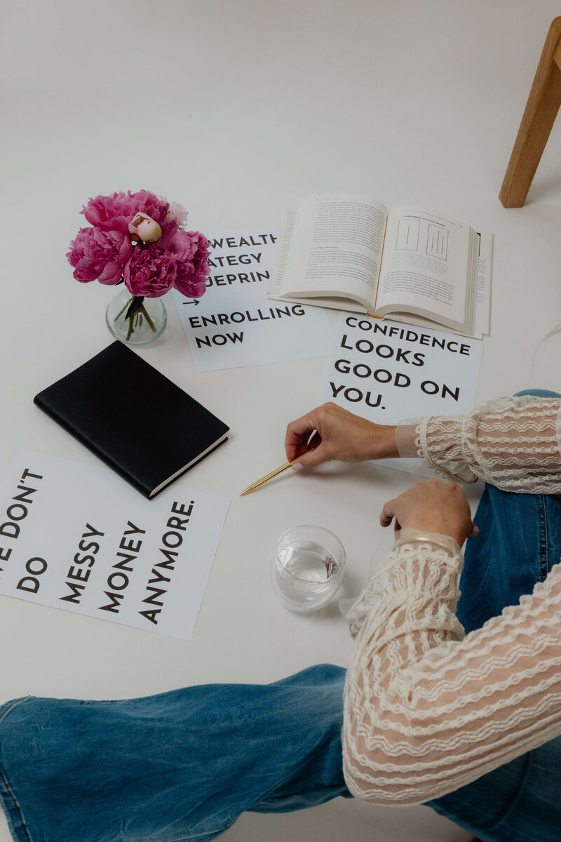 A women sitting on a floor with books and papers about confidence. 